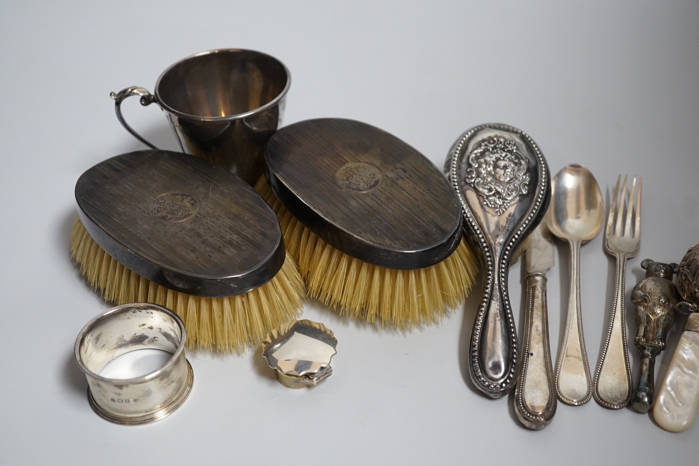 A mixed group of silverware including a pair of silver mounted clothes brushes, two rattles, a napkin ring, a christening trio and mug.